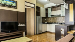 A modern kitchen with a built-in oven, a refrigerator, and a dining area with a bench and stools. - High Livin Apartment Baros (Cimahi)