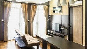 A modern hotel room with a sofa, a small table, a TV, and a wooden floor. - High Livin Apartment Baros (Cimahi)
