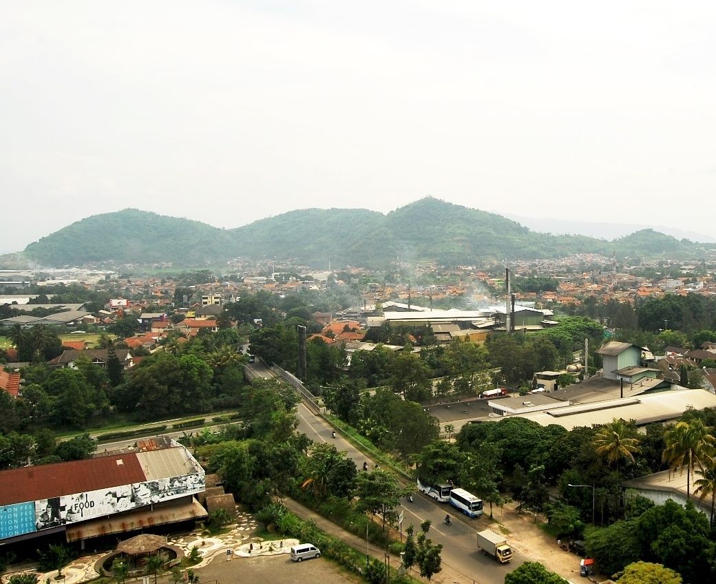 A town with a prominent industrial building, a large road, and surrounding greenery.