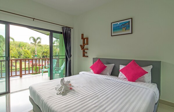 Habitación de hotel con cama, almohadas, un cuadro enmarcado y un balcón con vistas a zonas verdes.