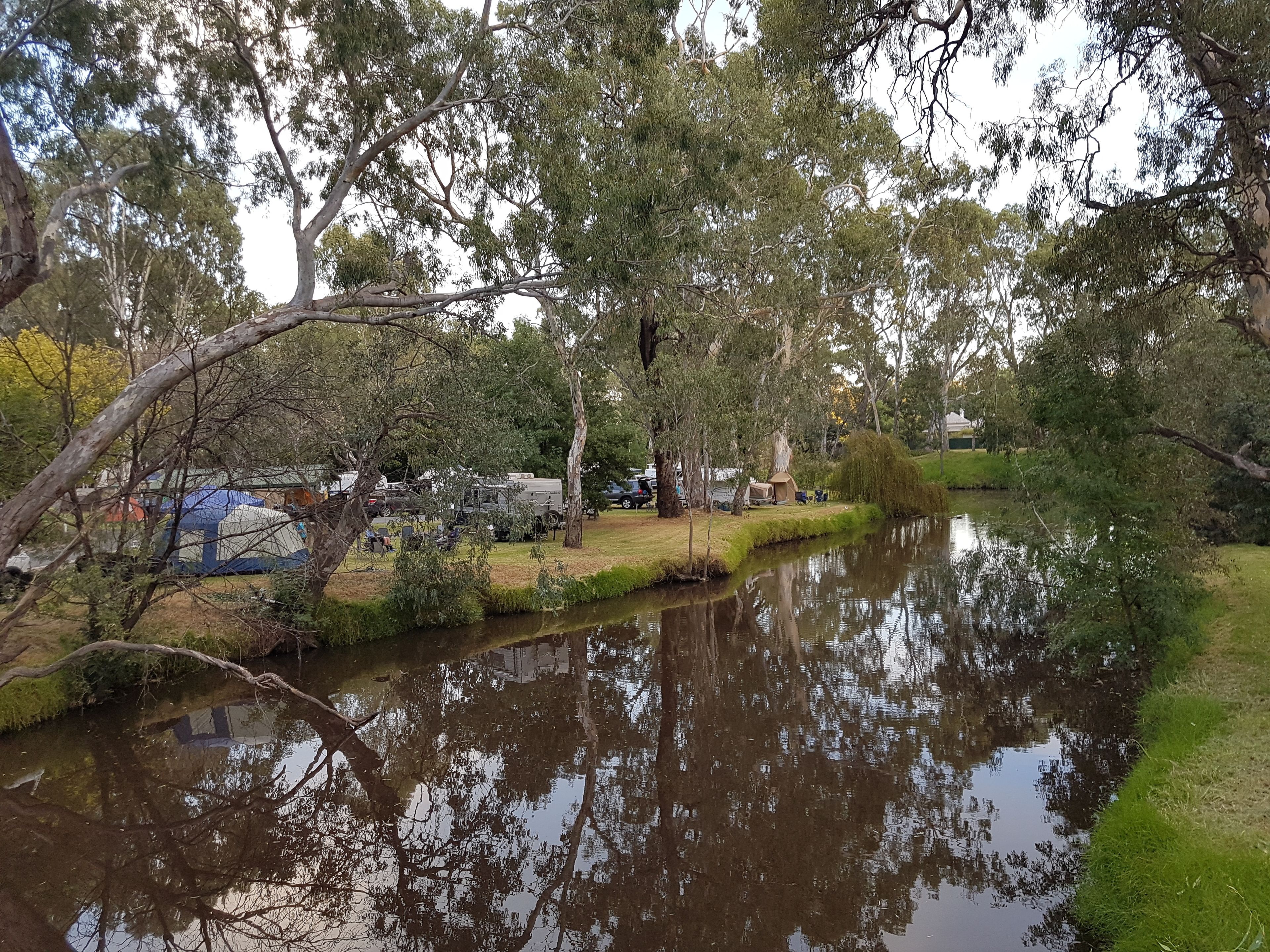 A serene riverside setting with trees and a tented area, likely a campsite.