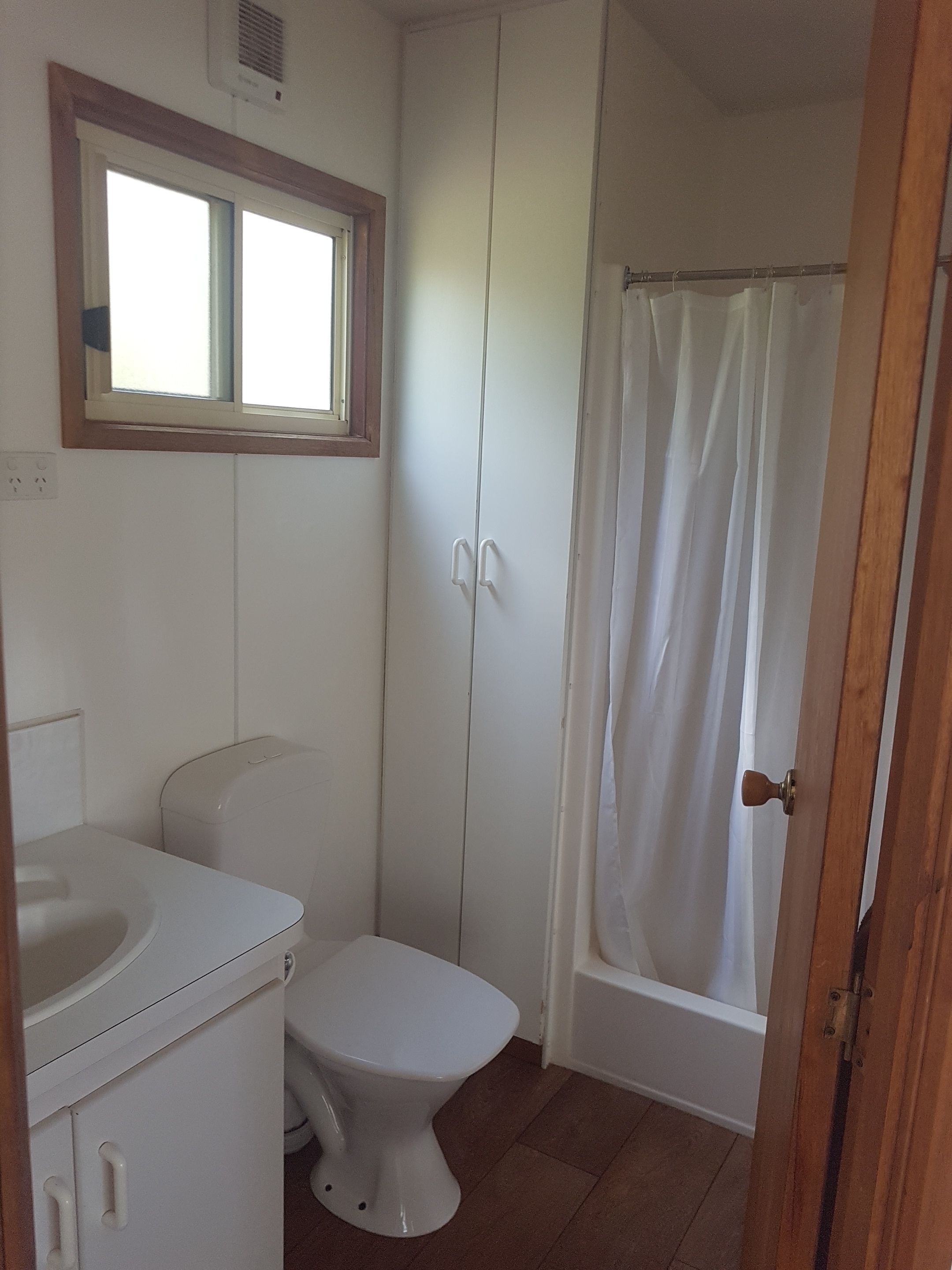 Un baño con inodoro, lavamanos, armario, cortina de ducha y ventana.