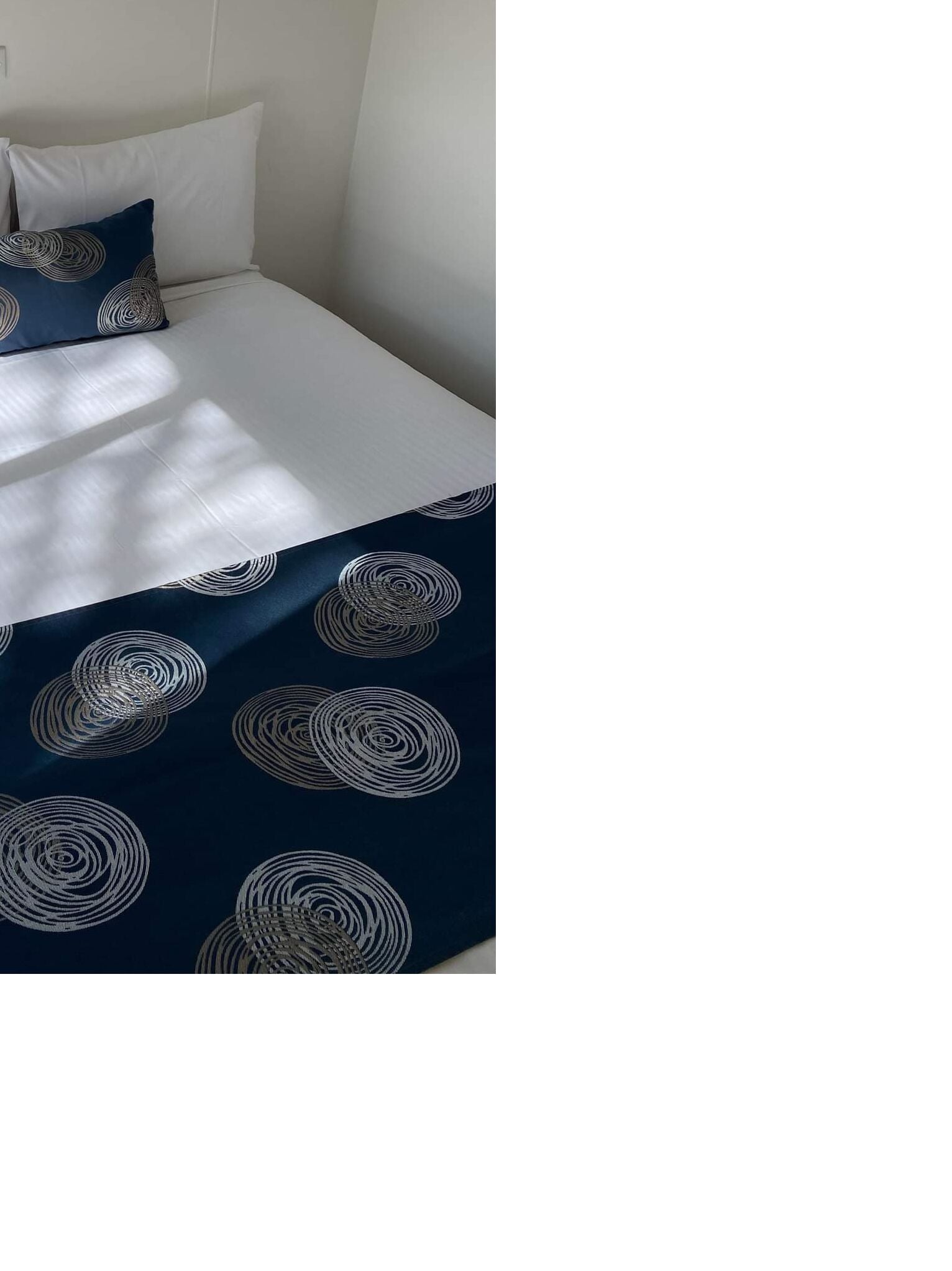 A bed with a white mattress and a navy blue blanket featuring circular patterns.