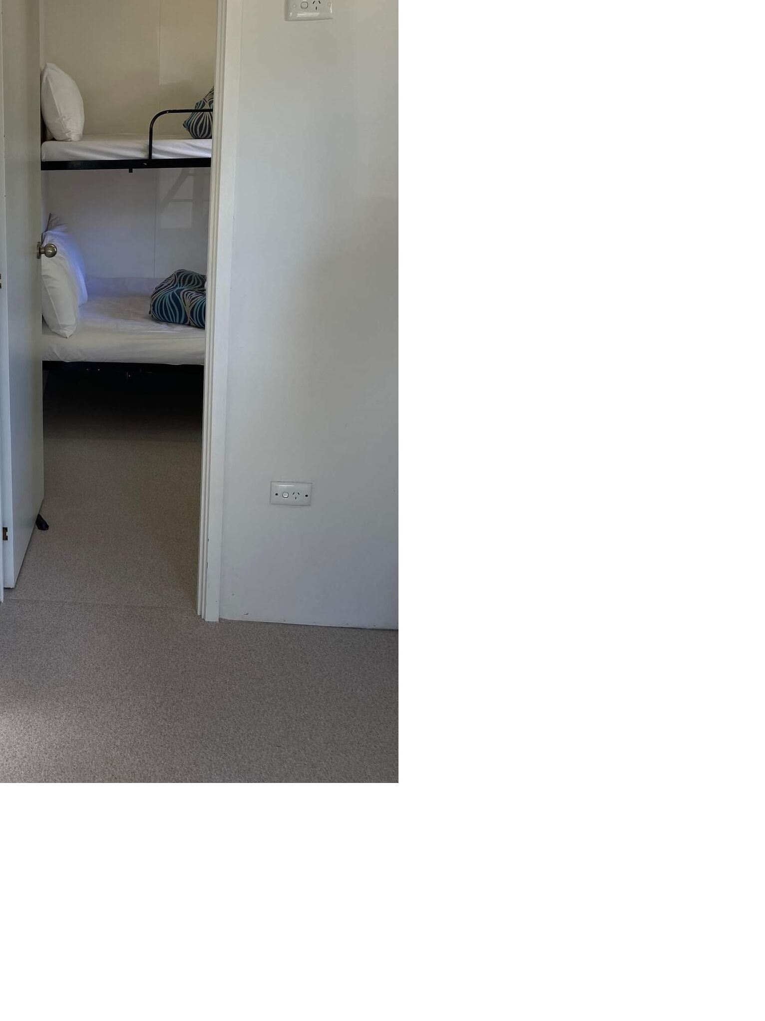 A room with two bunk beds, a white door, and a power outlet on the wall.