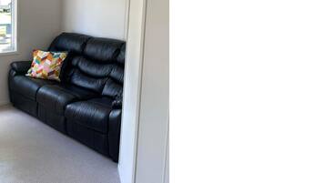 A room with a black leather sofa, a colorful cushion, a white door, and a carpeted floor.