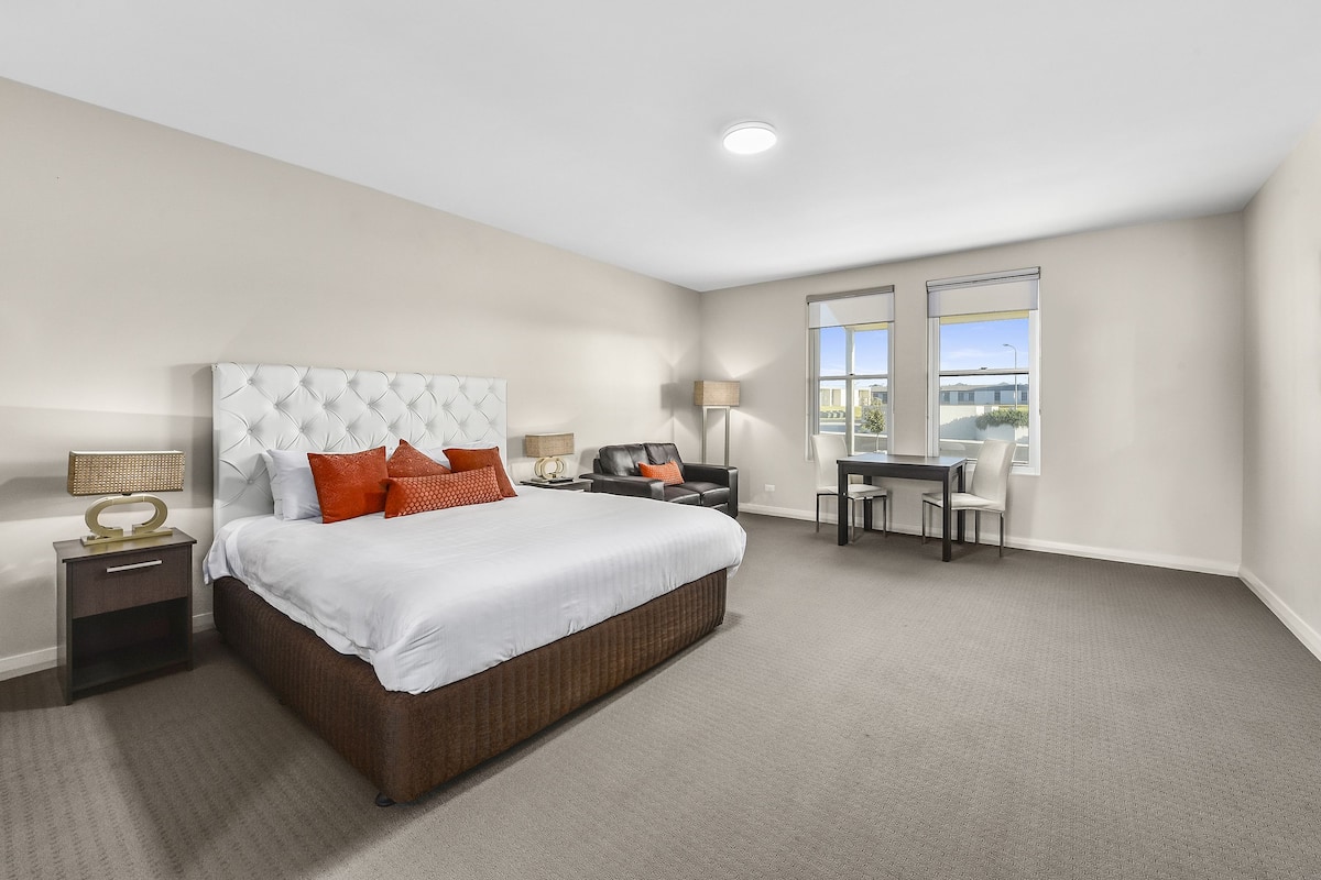 A bedroom with a large bed, a desk, and two windows.