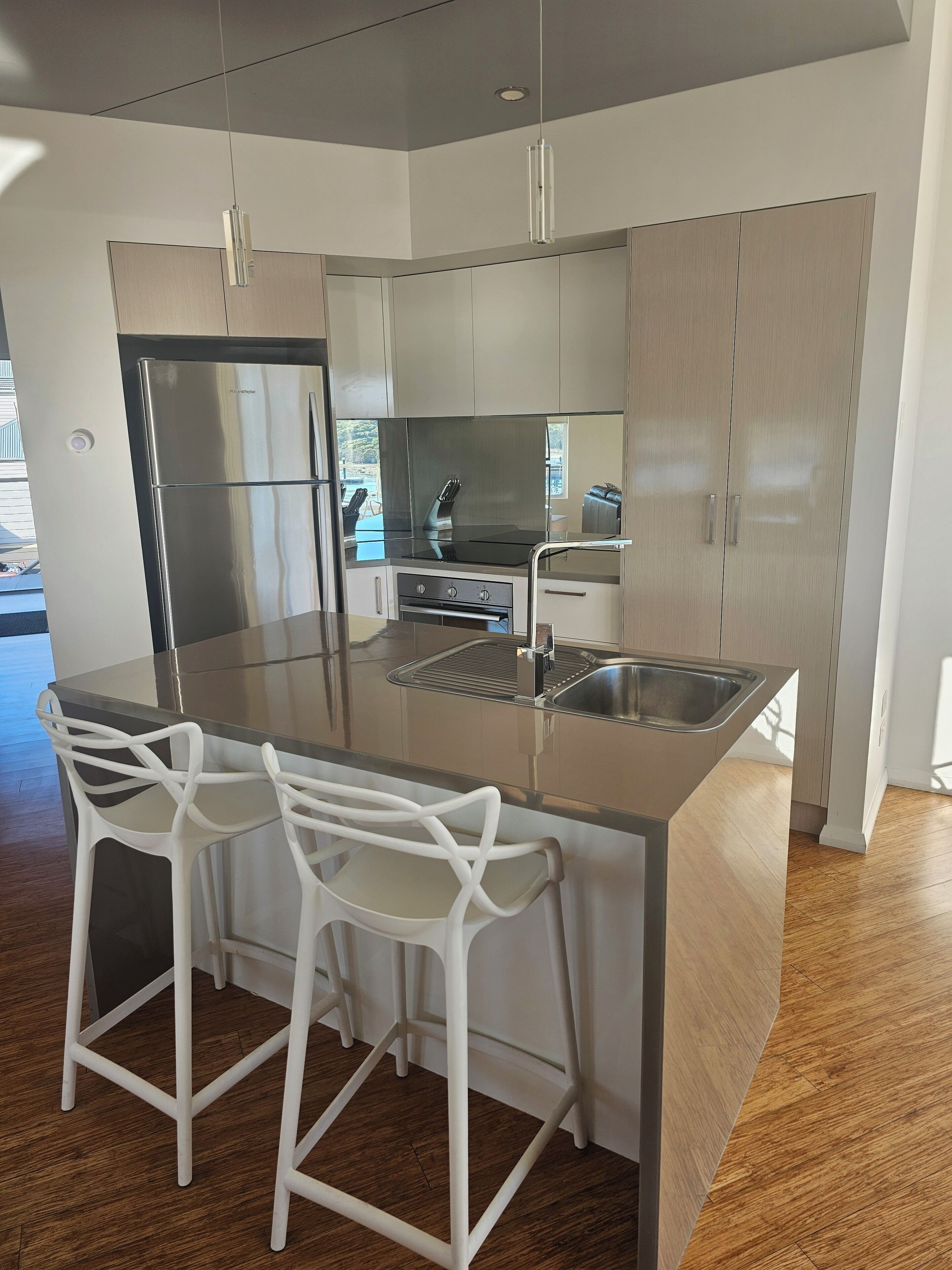 A modern kitchen with a large island, stainless steel appliances, and white bar stools.