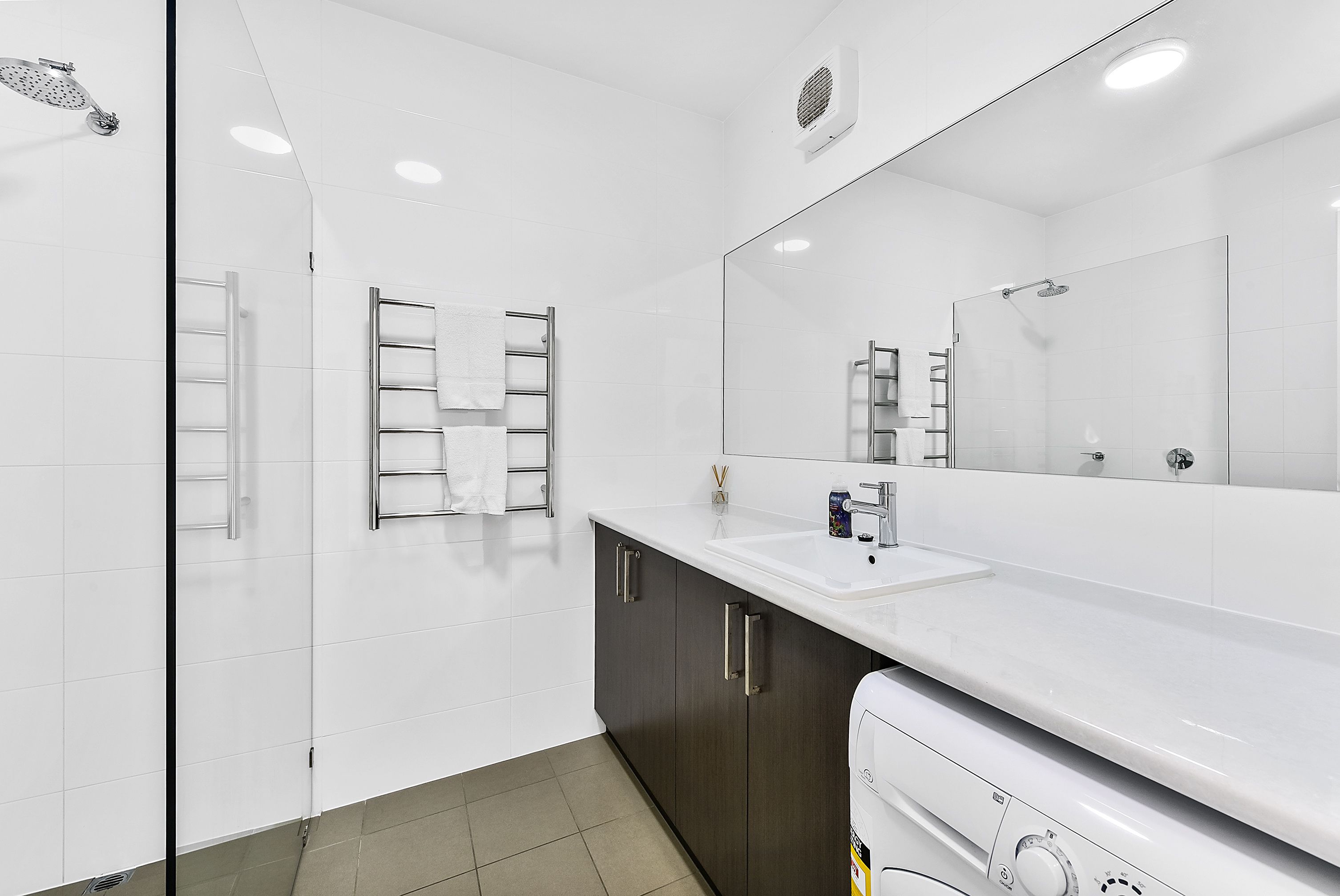 A modern bathroom with a glass shower enclosure, a white sink, and a large mirror.