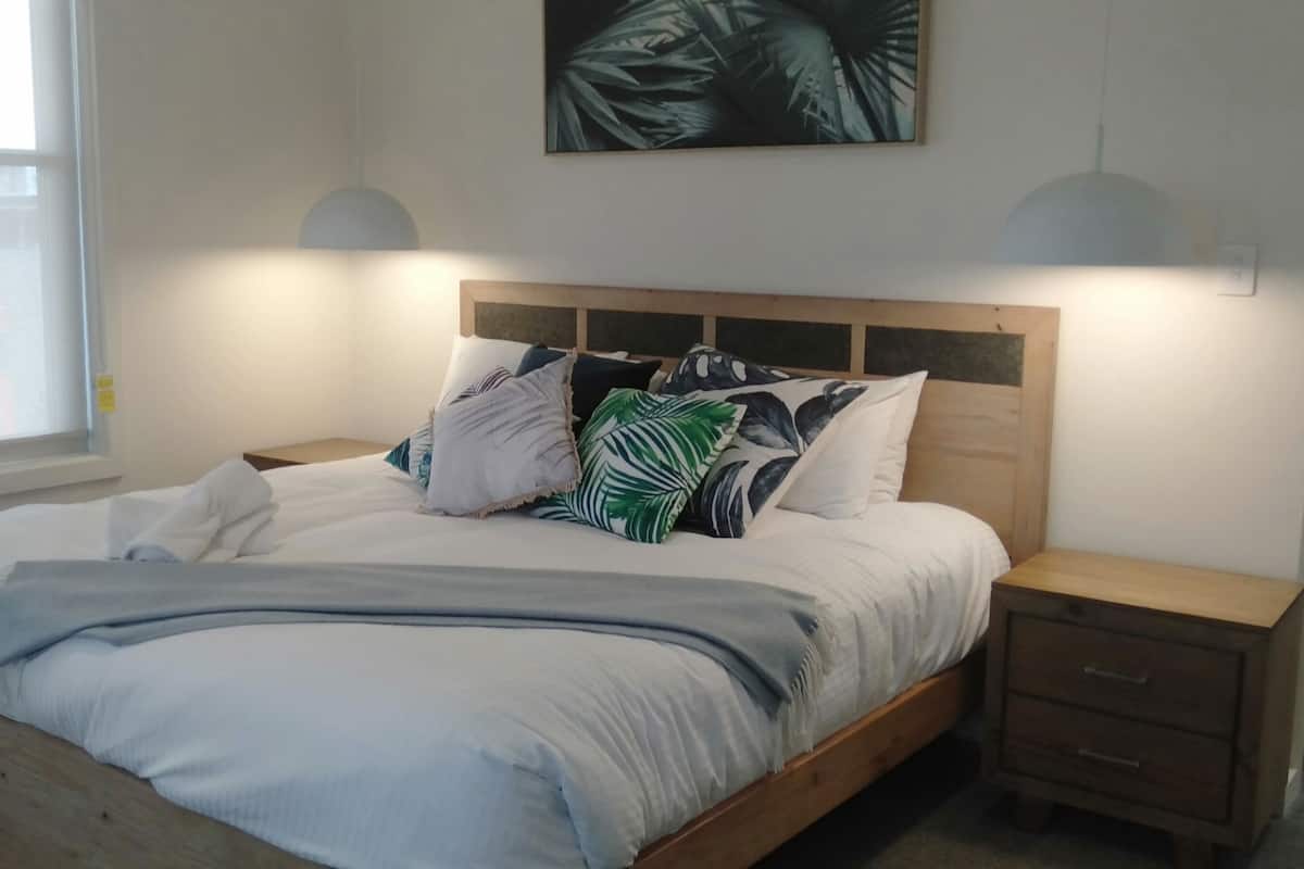 A bedroom with a wooden bed, white bedding, a large window, and a wall-mounted artwork.