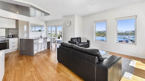 A modern kitchen with a dining area, a black leather sofa, and large windows with a view of the water. - Robe Marina Accommodation (Robe)