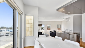 A modern kitchen with a large island, white cabinetry, and a view of the city through large windows. - Robe Marina Accommodation (Robe)
