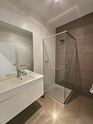 A modern bathroom with a glass-enclosed shower, a large mirror, and a white vanity.
