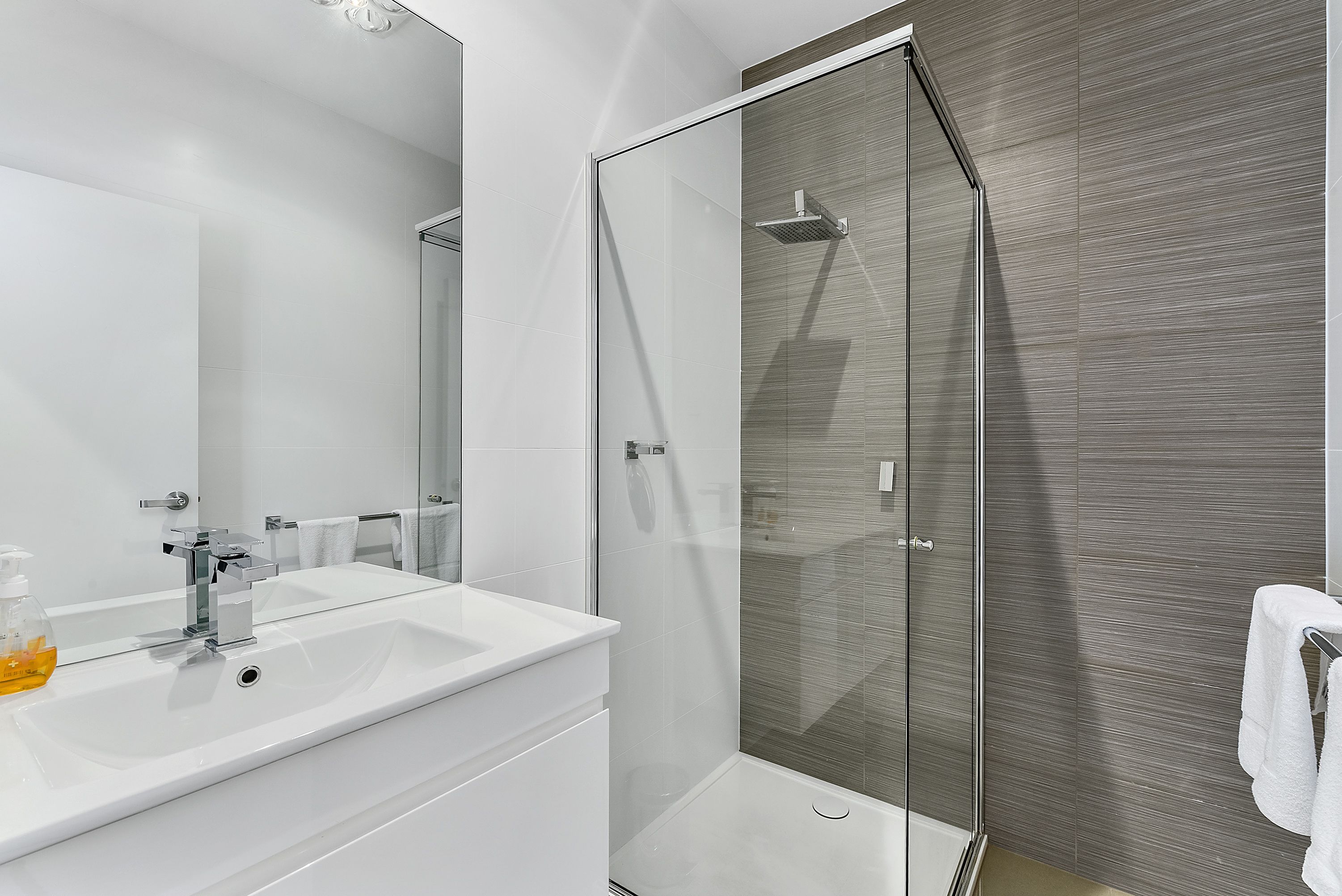 A modern bathroom with a white sink, a glass shower enclosure, and a large mirror.