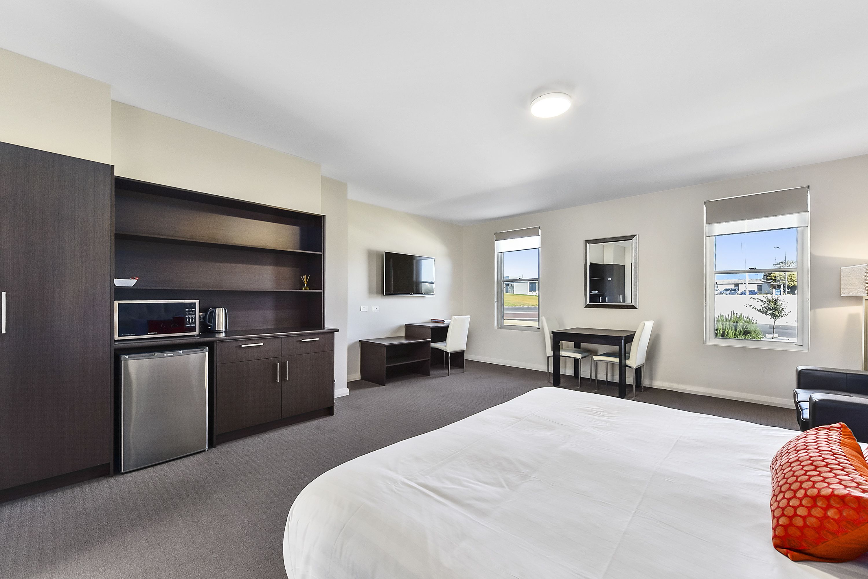 Una habitación de hotel moderna con una cama grande, un escritorio, una silla, un televisor y una kitchenette.
