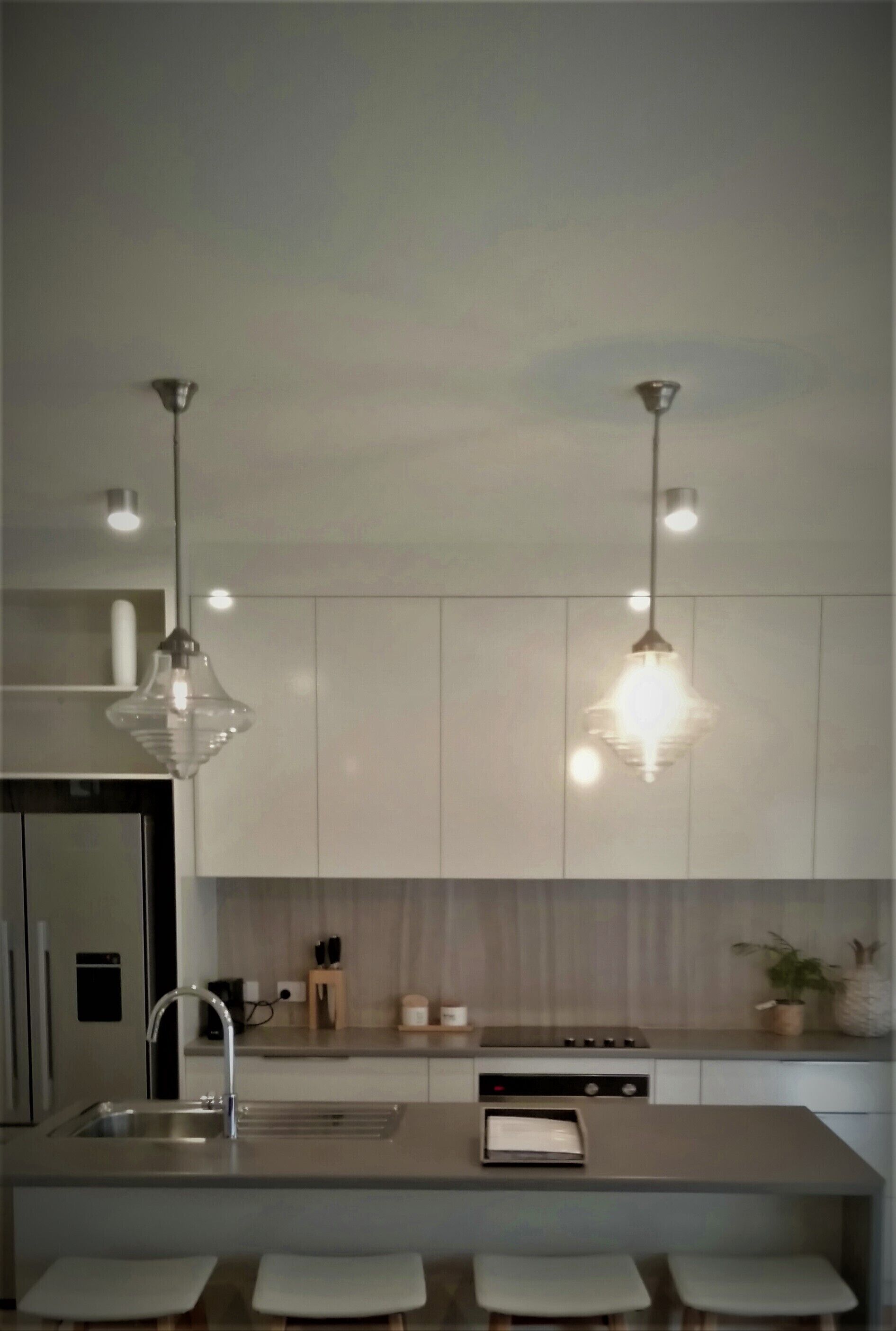 A modern kitchen with a stainless steel sink, a built-in oven, and a countertop with a toaster. There are two pendant lights hanging above the sink.
