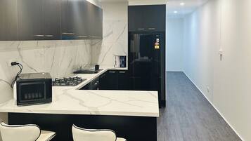 A modern kitchen with dark cabinets, a marble backsplash, a black refrigerator, and a central island with two white bar stools.