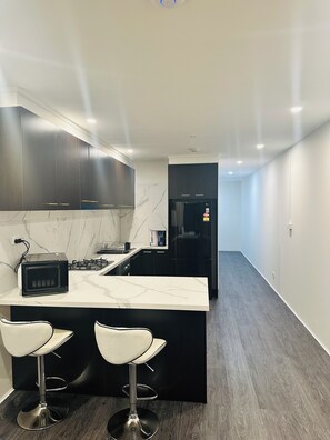 A modern kitchen with dark cabinets, a marble backsplash, a black refrigerator, and a central island with two white bar stools.