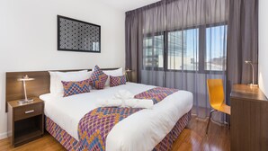 A hotel room with a large bed, a nightstand with a lamp, a chair, and a desk. - Exodus Dandenong Apartment Hotel (Melbourne)