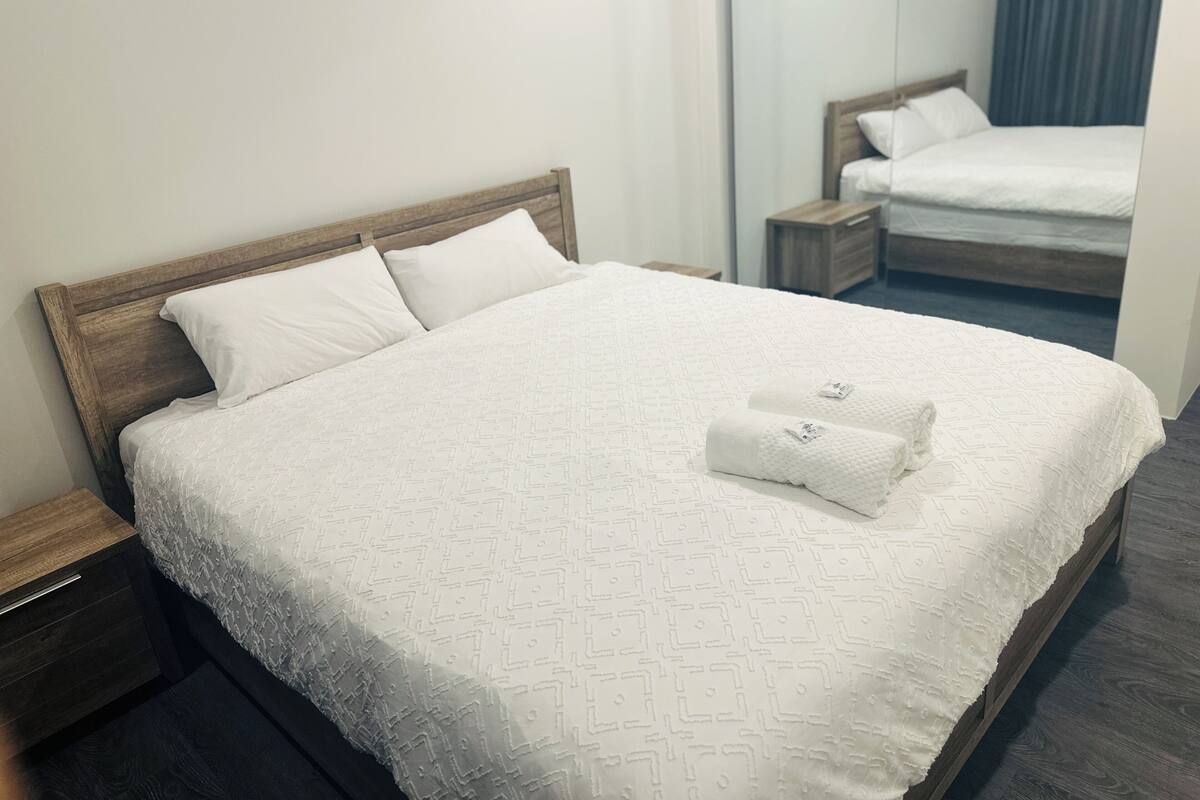 A neatly made bed with a wooden headboard, white linens, and a folded towel on the bed.