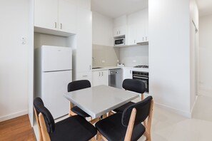 A compact kitchen with white cabinets, a built-in microwave, a dishwasher, and a stove. There is a small dining table with four chairs. - Exodus Dandenong Apartment Hotel (Melbourne)