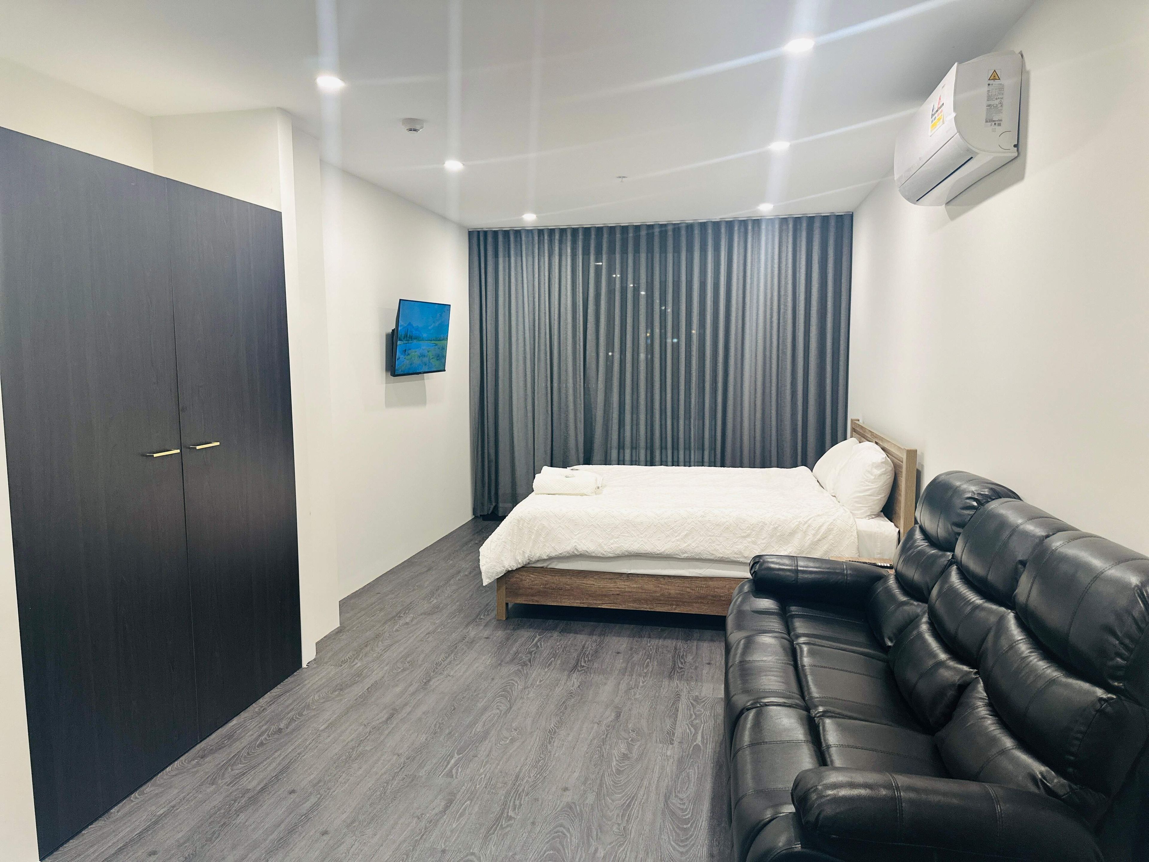 Een slaapkamer met een bed, een donkere kast, een leren bank, een tv aan de muur en een airconditioning.