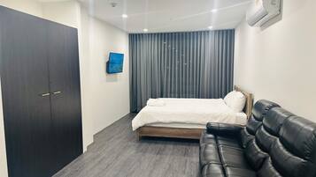 Een slaapkamer met een bed, een donkere kast, een leren bank, een tv aan de muur en een airconditioning.