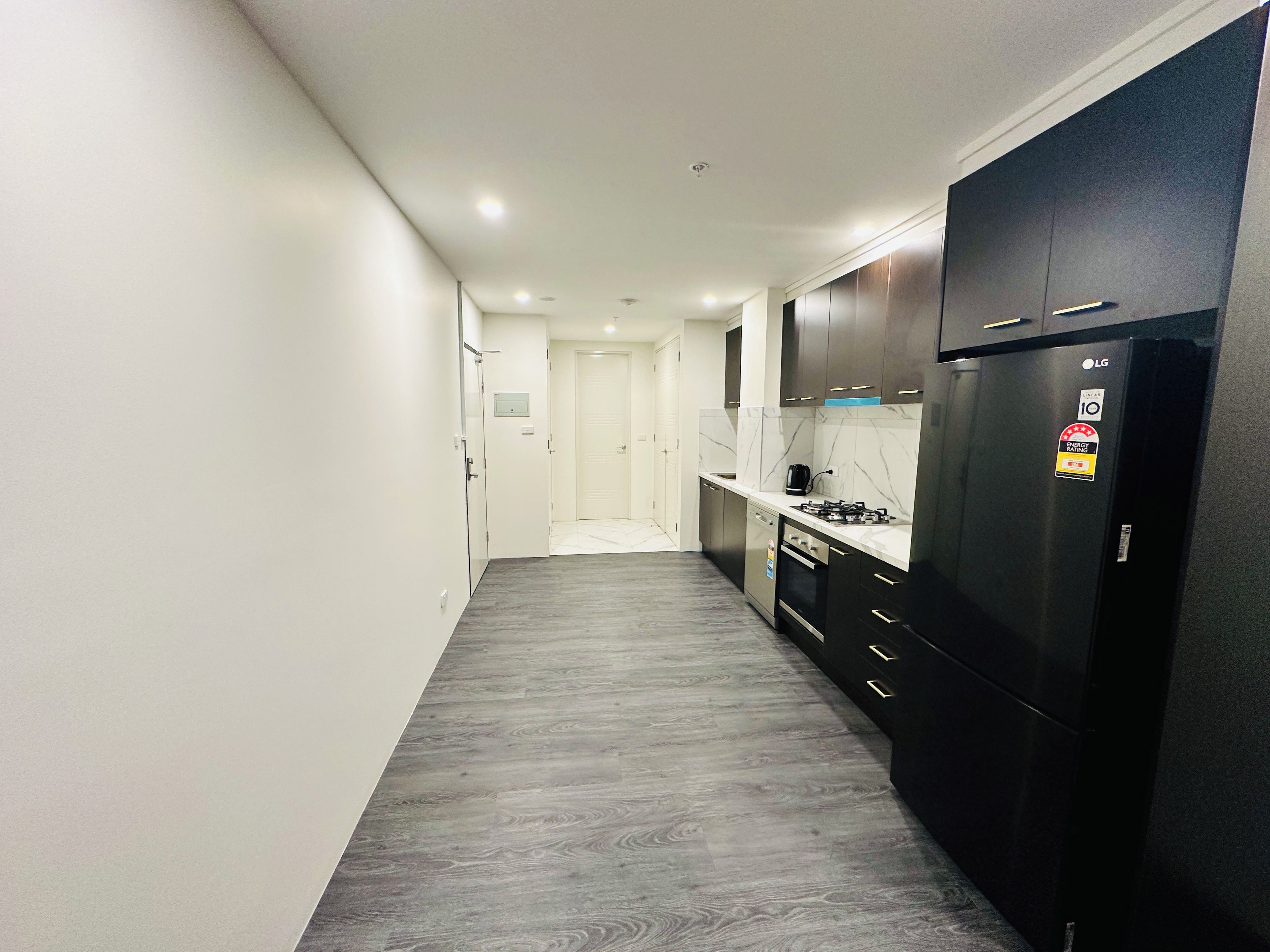 A narrow hallway leading to a kitchen with dark cabinets, a black refrigerator, and a gas stove.
