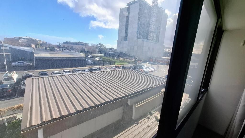 Vista desde una ventana sobre un estacionamiento con varios autos y un edificio en construcción al fondo.