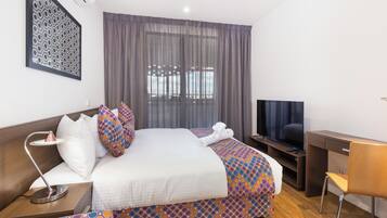 Habitación de hotel con cama, escritorio, silla, televisor y ventana con cortinas.