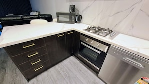 A modern kitchen with dark cabinets, a microwave, a gas stove, an oven, and a dishwasher. - Exodus Dandenong Apartment Hotel (Melbourne)