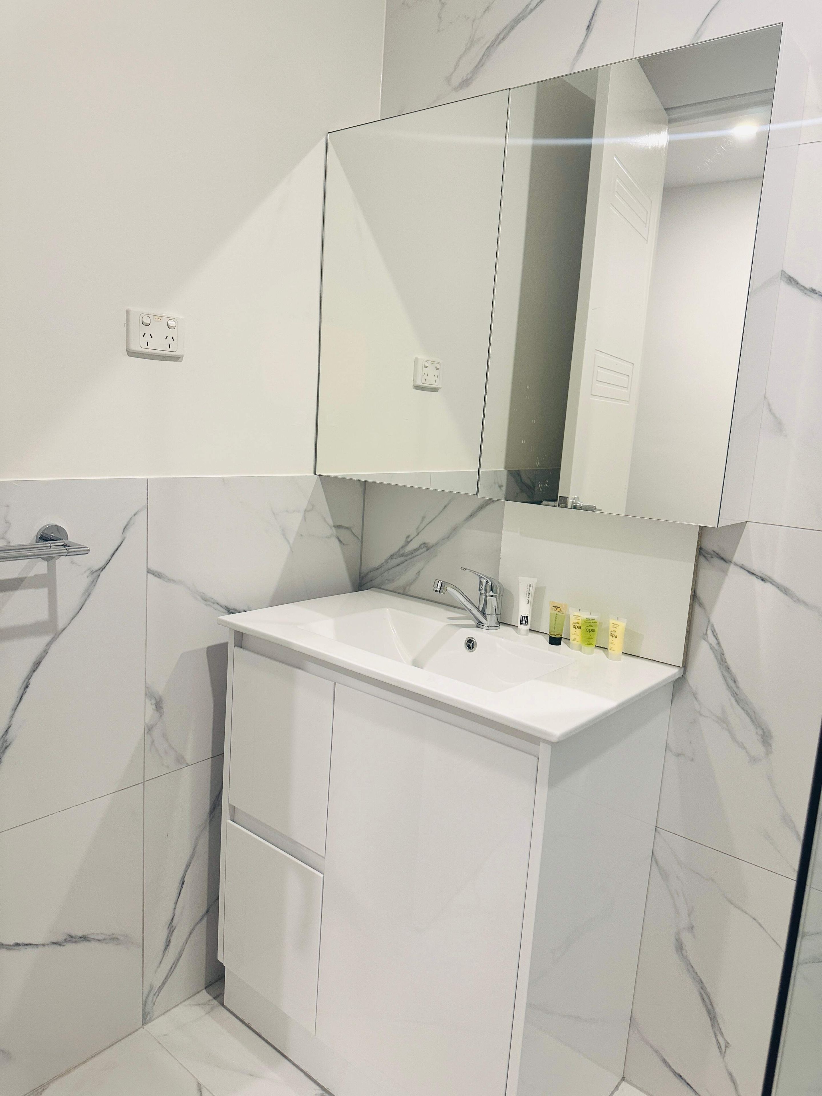Un bagno moderno con un lavandino bianco, uno specchio e pareti con motivo marmorizzato.