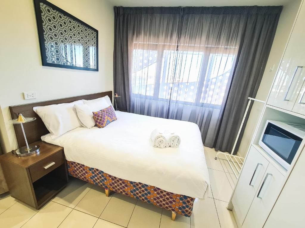 Quarto de hotel com cama, mesa de cabeceira, televisão e janela com cortinas.
