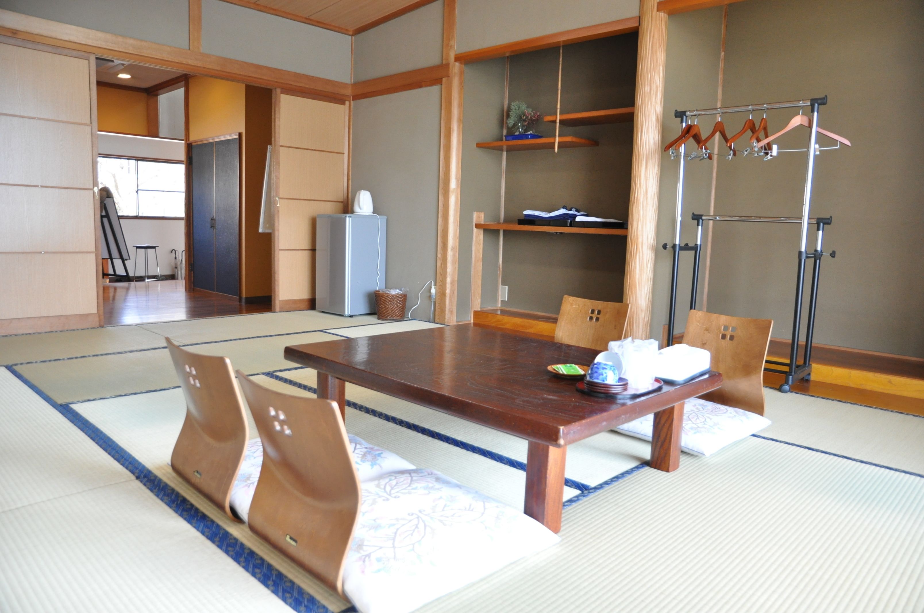 Une pièce traditionnelle japonaise avec un sol recouvert de tatamis, une petite table en bois, des tatamis, un porte-vêtements suspendu et une porte coulissante donnant sur une autre pièce.