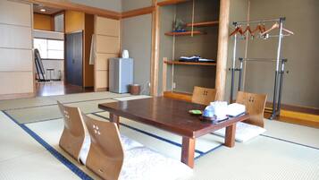 Une pièce traditionnelle japonaise avec un sol recouvert de tatamis, une petite table en bois, des tatamis, un porte-vêtements suspendu et une porte coulissante donnant sur une autre pièce.