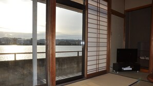 A room with tatami flooring, a sliding shoji screen, a television on a black stand, and a view of a river with buildings across it. - Kahan no Yado Karatsu Castle (Karatsu)