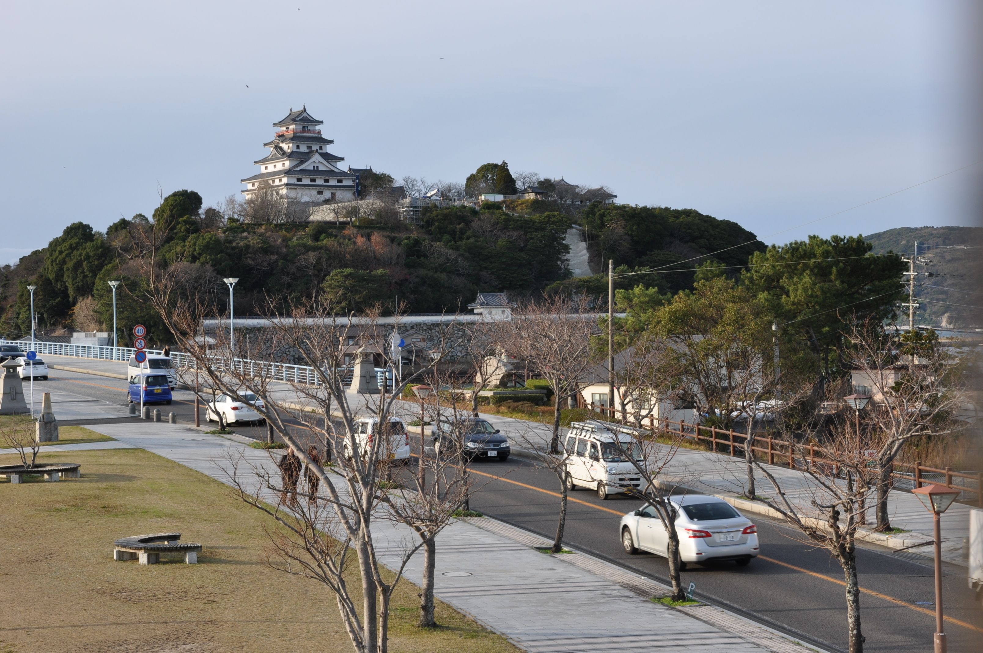 Una carretera con coches, un camino peatonal y un edificio tradicional grande en una colina.