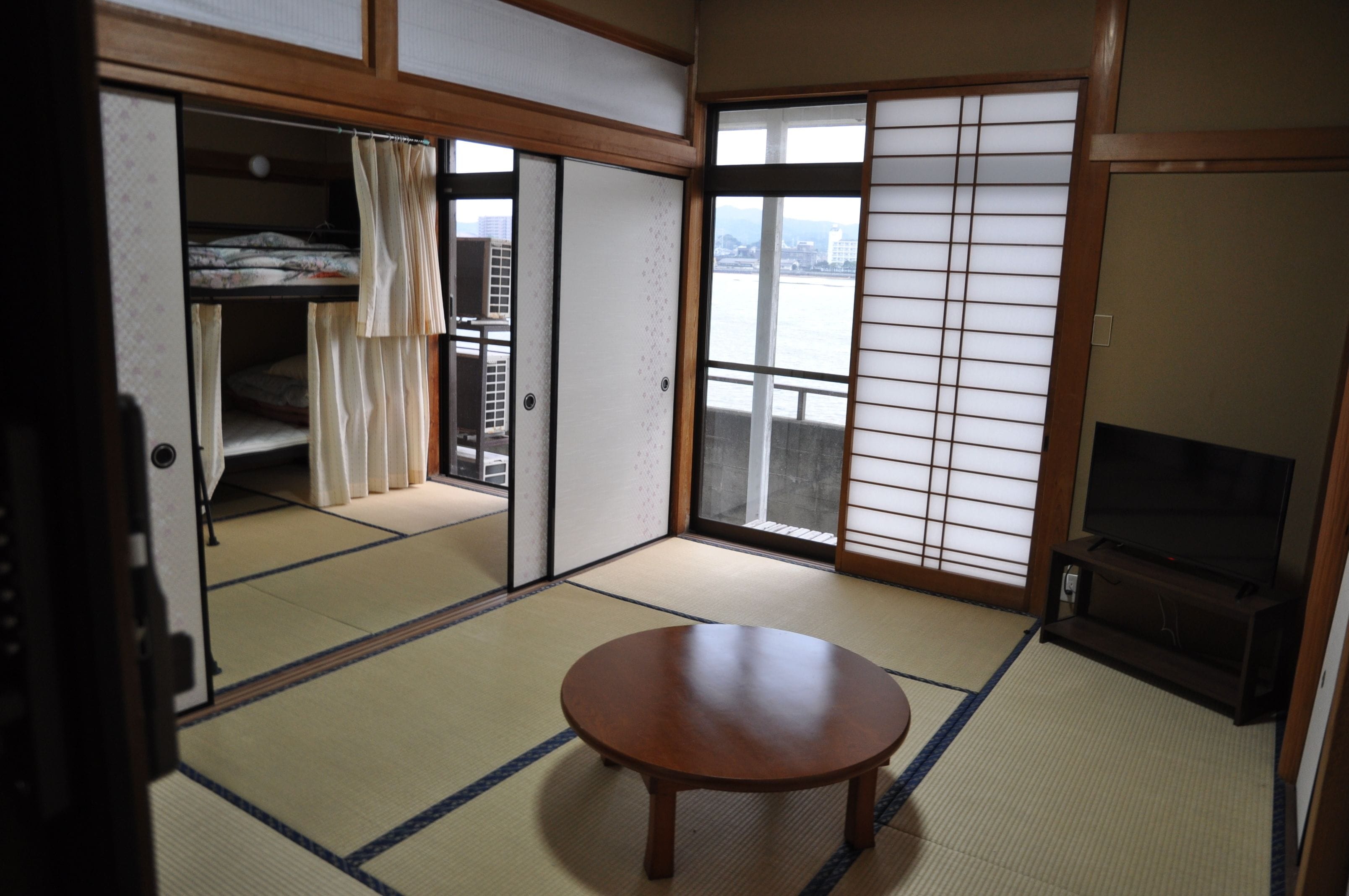 A traditional Japanese room with tatami flooring, a sliding door, a bed, and a television.