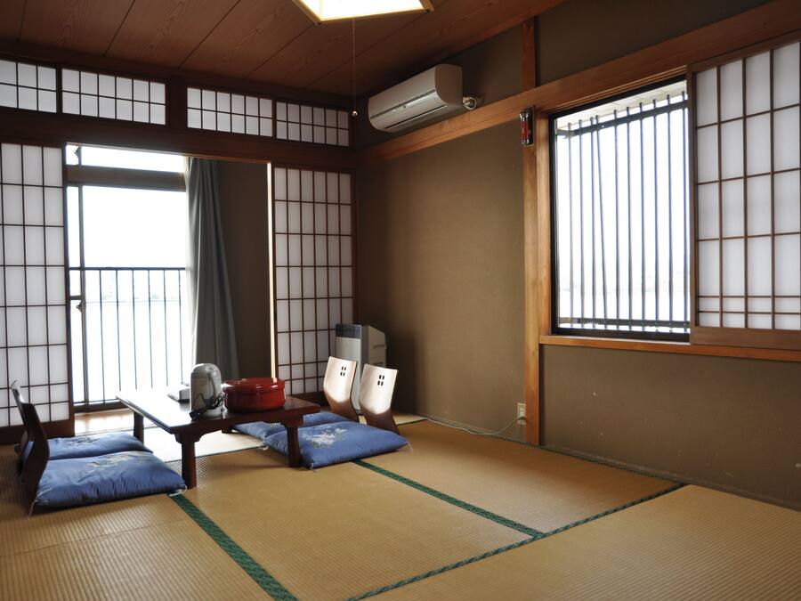 A traditional Japanese room with tatami flooring, a low table with cushions, a futon, and sliding doors.