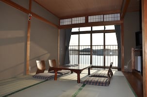 Una habitación japonesa tradicional con suelo de tatami, una mesa baja, cojines y vistas al mar a través de amplios ventanales.