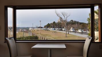 Vista desde una ventana de una habitación con dos sillas y una mesita. Se ve un estacionamiento con coches y un edificio con una estructura similar a una pagoda.