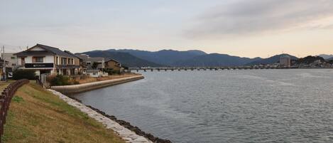 A riverside view with a bridge, houses, and mountains in the background.
