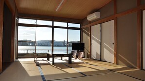 A tatami mat room with a large window overlooking a body of water and distant buildings. - Kahan no Yado Karatsu Castle (Karatsu)
