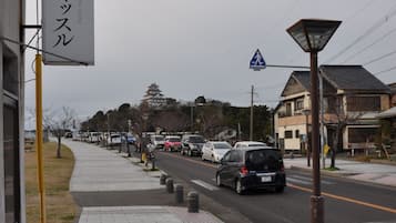 Une rue où les voitures sont garées le long du trottoir, un panneau indiquant un passage pour piétons et un bâtiment avec une enseigne en japonais.