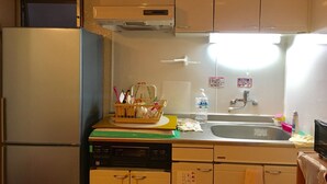 A compact kitchen with a refrigerator, a microwave, and a sink. There are cabinets above the sink and a small window above the refrigerator. - Women's Guest House Fukutomi (Naha)