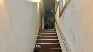 A narrow stairway with wooden steps and a handrail, leading to a landing with a door. - Women's Guest House Fukutomi (Naha)