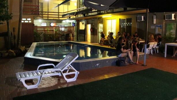 Zona de piscina al aire libre con sillones de descanso y un grupo de personas sentadas alrededor de una mesa.