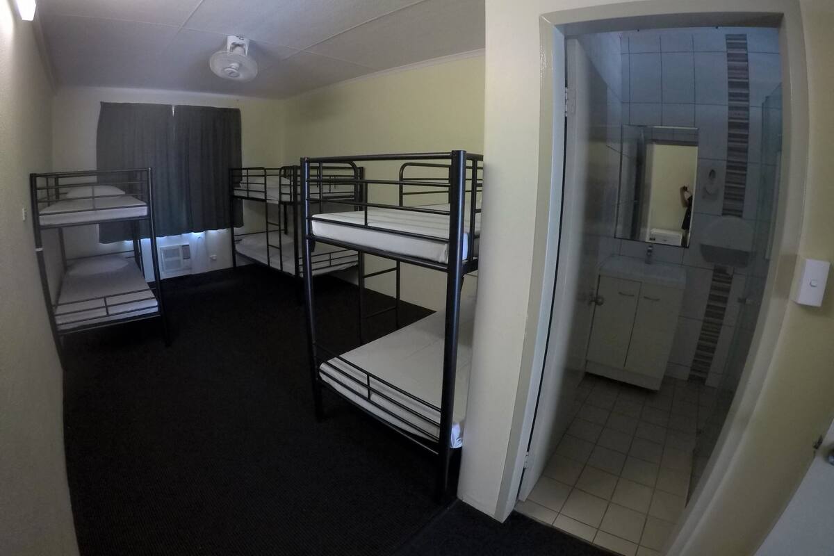 A dormitory room with bunk beds, a ceiling fan, a mirror, and a bathroom visible through an open door.