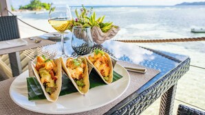 Una mesa con tacos, una copa de vino blanco y un florero decorativo con flores.