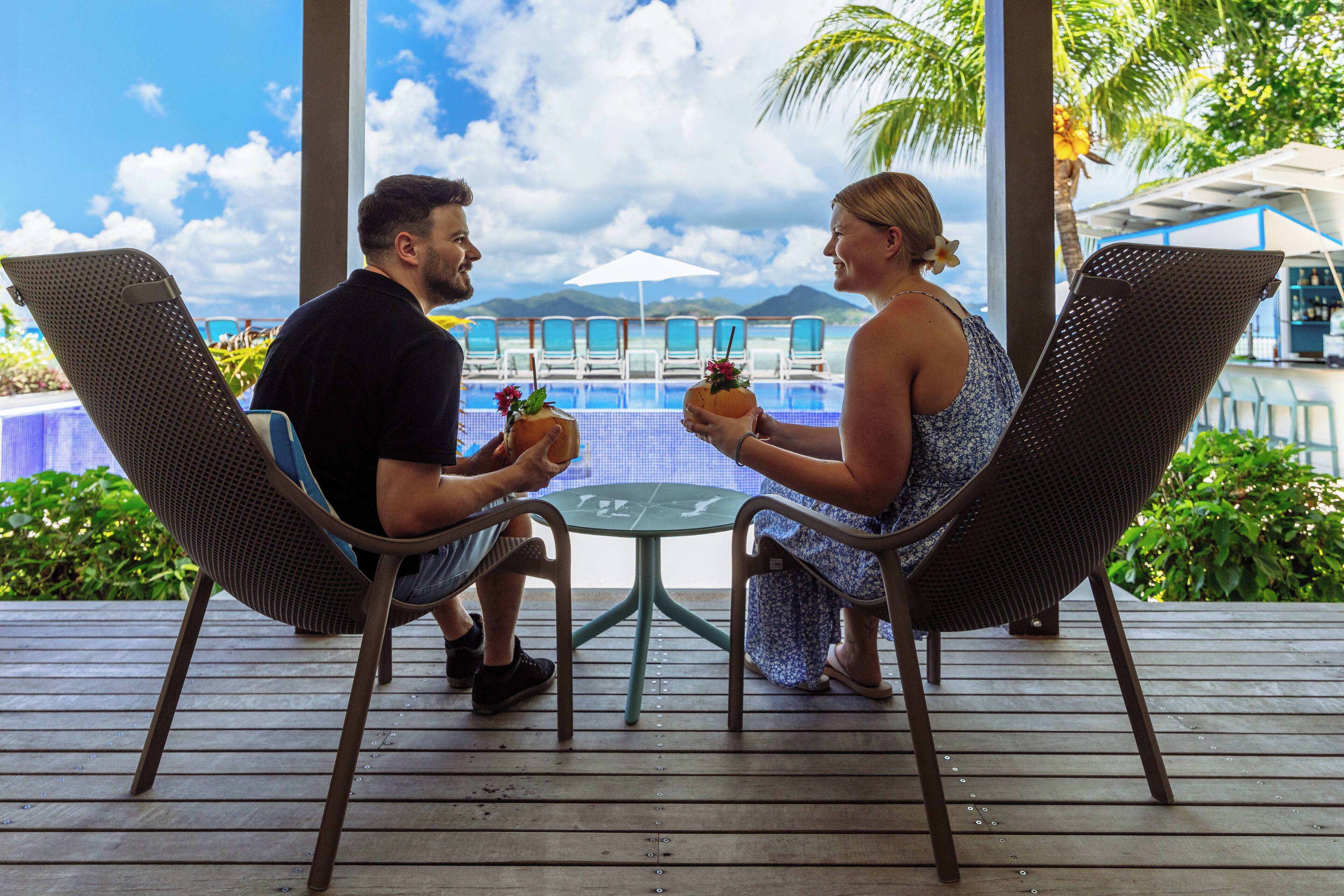 Two people seated at a table with a view of a pool and mountains in the background.