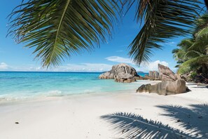 A beach with white sand, clear turquoise water, and large rock formations. - Le Nautique - Luxury Waterfront Hotel (La Digue)
